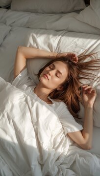 A young woman relaxes comfortably in bed surrounded by soft white bedding, enjoying a peaceful morning at home.