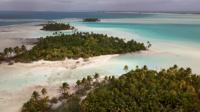 Aerial drone shot moving forward over lush tropical palm tree motus and the shallow, brilliant turquoise waters of the Blue Lagoon in Rangiroa atoll