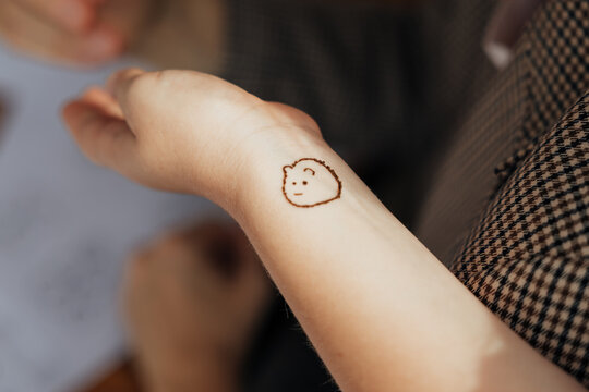 Close-up of a small hand-drawn henna face motif on a person&rsquo;s wrist, featuring a simple smiling expression and rounded outline in warm natural light