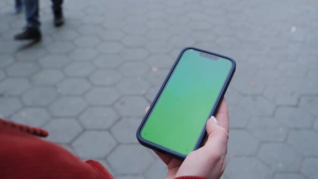 Female hand holding smartphone green screen gadget in street at daytime, walking crowded crosswalk with phone chroma key display. High quality 4k footage