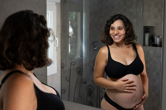 Happy pregnant woman admiring her baby bump in mirror