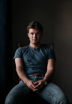 Serious young man sits for a dramatic portrait in dark room