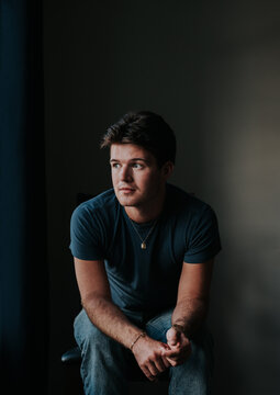 Thoughtful young man sitting indoors looking away from the camera