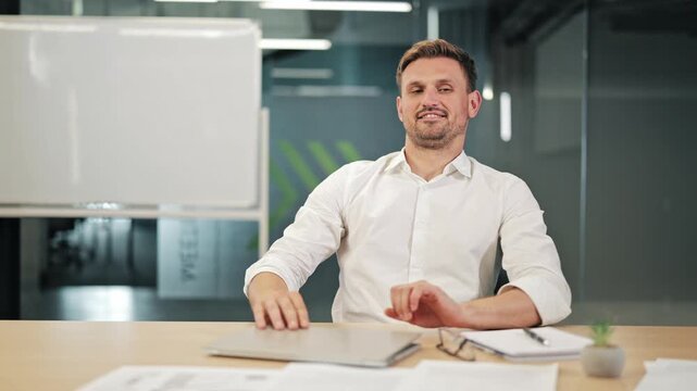 Happy businessman finishing work project and closing laptop in modern office, leaning back in chair with relieved smile, celebrating successful end of workday and task completion