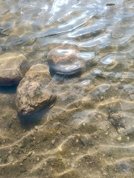Clear water over rocks ripple patterns shallow riverbed light reflections across wet stones under sunlit surface, with water, rock, stone, river detail, showing stream, shallow, clear, reflection