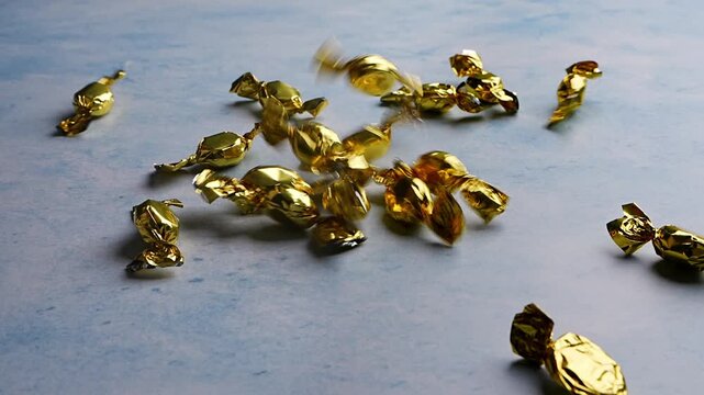 Goldenin shiny wrappers candies slowly falling onto table. Close up. Festive food, sweets, celebration, indulgence, confectionery, party treats. 