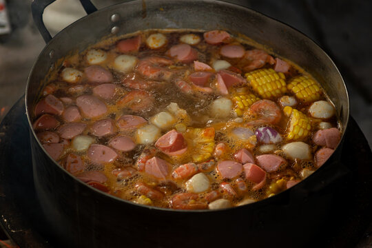 Detailed top view of delicious boiling soup with fresh shrimps, sweet corn, sausages and fish balls