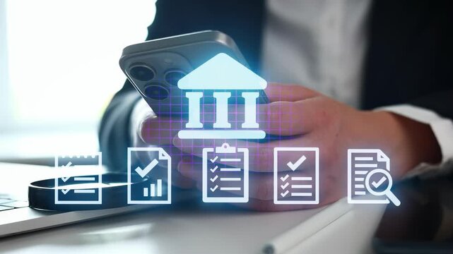 A person is holding a smartphone while sitting at a desk. Financial and planning icons are displayed on the screen. A laptop is on the desk.