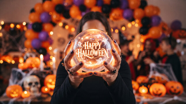 Person holding a glowing crystal ball with happy halloween text in a festive decorated room