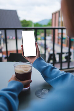 Vertical mockup image of a woman holding and using mobile phone with blank desktop screen while drinking coffee in cafe