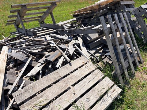 Pile of old weathered wooden planks and dismantled pallets on green grass
