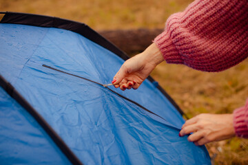Close-up of woman hands zipping up blue tourist tent during fall outdoor camping trip © cenchild