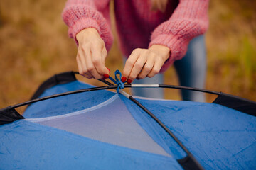 Close-up of woman hands tying knot on camping tent frame in woodland campsite © cenchild