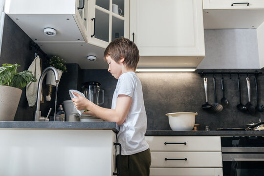 Boy washing dishes in kitchen, learning domestic responsibility