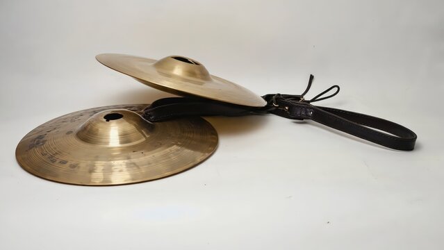 Close-up of two brass cymbals held by a black leather hand strap, musical percussion instruments for studio photography.