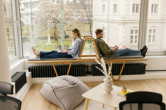 Man and woman use laptop and tablet by a large office window