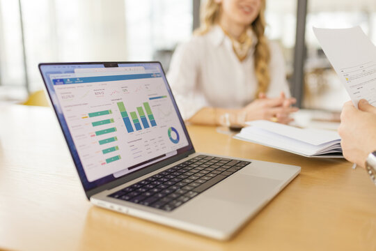 Colleagues analyze financial charts on a laptop during a meeting