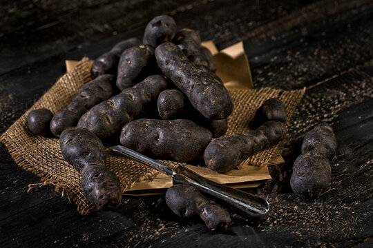 Blue violet potatoes and peeler on brown paper, jute and dark wood