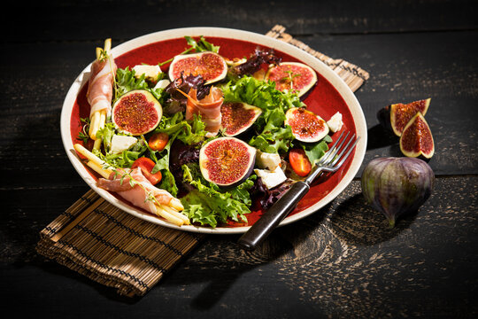 Mixed salad with figs, tomatoes, sheep cheese, grissini with ham on plate