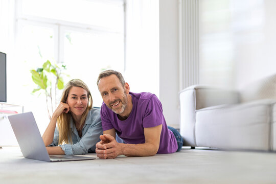 A mature couple uses a laptop on the living room floor