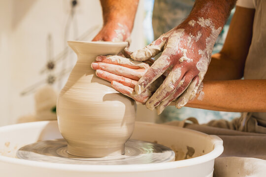 Teacher guides student shaping clay vase on pottery wheel indoors