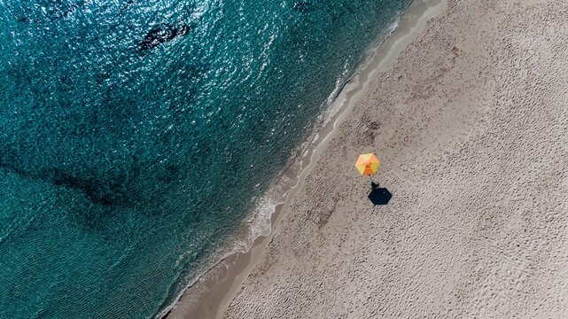 Turquoise ocean water meets a sandy beach with a yellow umbrella