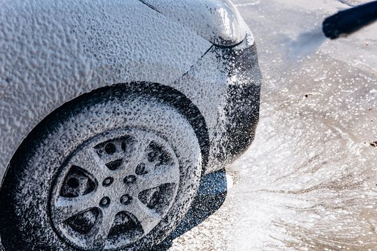 A pressure washer sprays thick foam onto a car wheel during a wash