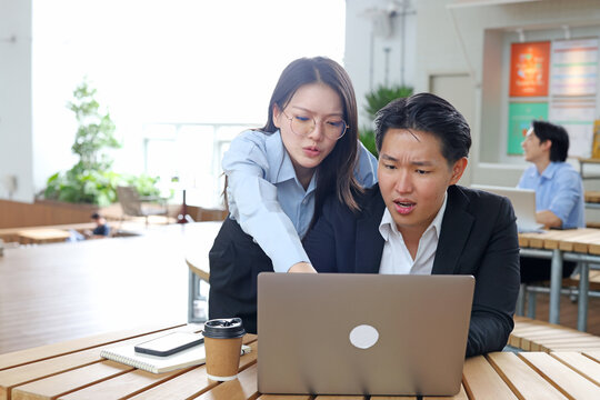 Two Concerned Business Professionals Looking at Laptop Screen in Modern Office