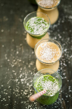 Glasses of spinach smoothie and mango smoothie with desiccated coconut on wooden table, elevated view