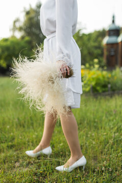 Side view of woman in white bridal dress holding fluffy dry bouquet outdoors.