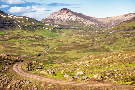 Winding gravel road through green valley to rhyolite mountain in East Iceland