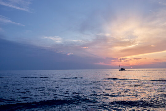 A sailboat sails on the Adriatic Sea during a colorful sunset