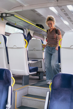 Smiling woman with backpack walks down the aisle of a train carriage