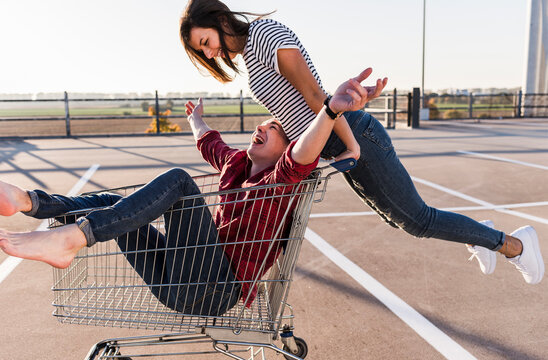 Playful young couple with shopping cart on parking level