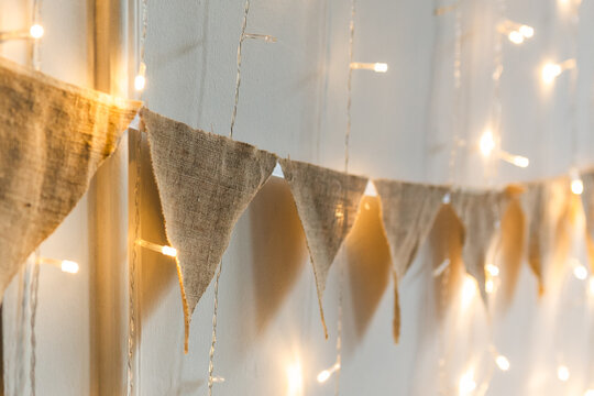 Burlap triangle flag garland and glowing warm fairy lights hanging on wall as festive holiday decor.