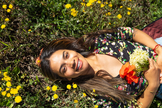 Smiling woman lies in a meadow holding a red poppy and white flower
