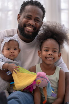 A devoted diverse father entertains his kids with a soft doll on the floor in a warm living room, showing devoted fatherhood in a warm welcoming home ideal for parenting and wellbeing.