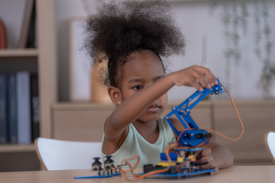A creative little student tinkers with a blue robot arm at the table at a bright learning table at home, full of curiosity and focus with a clean modern aesthetic.