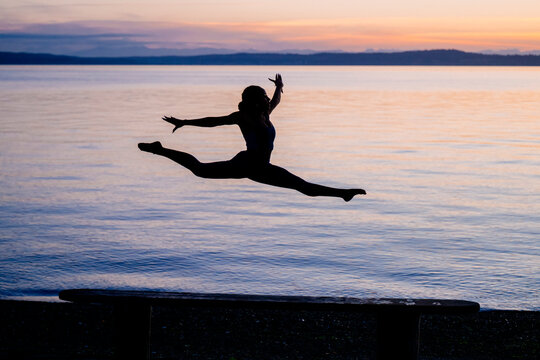 Hispanic woman performing acrobatic split jump outdoors by a lake