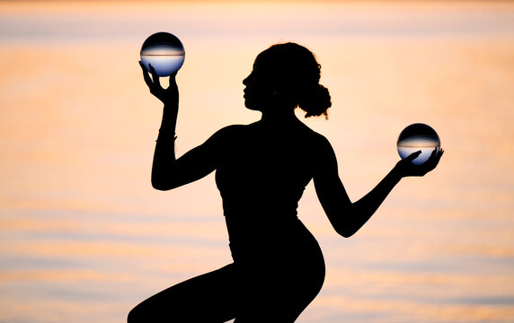 Silhouette of Hispanic woman performing yoga with glass balls
