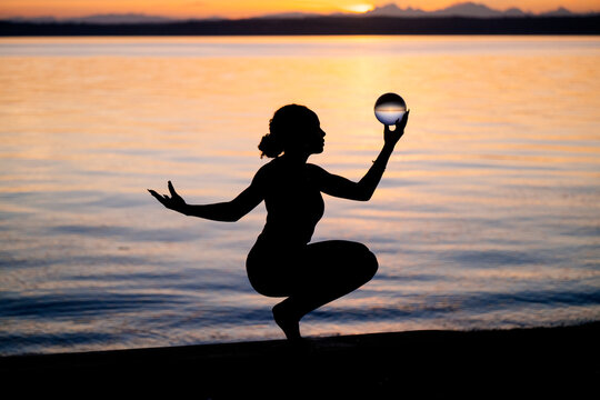 Silhouette of Hispanic woman balancing yoga pose with glass sphere