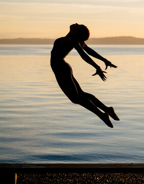 Hispanic woman jumping in yoga pose at lake during sunset