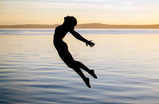 Hispanic woman jumping in yoga pose by lake at sunset