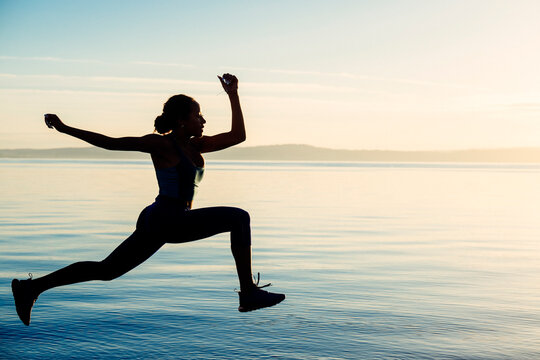 Hispanic woman jumping in silhouette outdoor exercise pose by lake