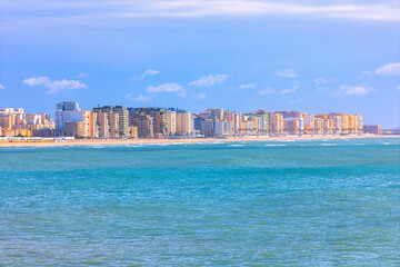Cadiz city in  Spain, presents striking coastal view where modern high-rise apartments line beachfront of Playa de la Victoria. Turquoise waters of Atlantic Ocean lap gently against shore © Leilani