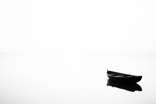 Extreme minimalist high key black silhouette of a single empty rowboat on a seamless white void