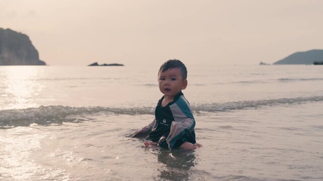 Toddler enjoying water play at beach shore during warm sunset family vacation.