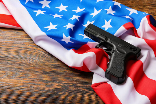 Gun control and second amendment debate, black handgun resting on a folded United States flag on a rustic wooden table American politics
