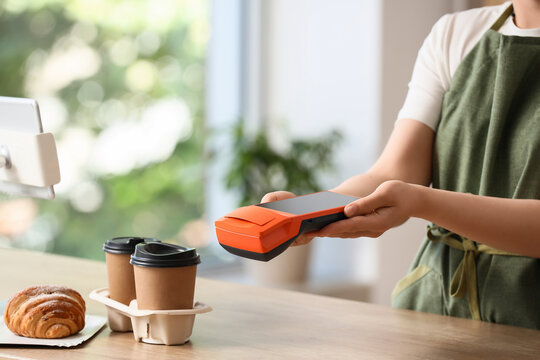 Contactless payment and digital transaction, barista holding a mobile card terminal for customer checkout in a coffee shop with takeaway coffee and pastry