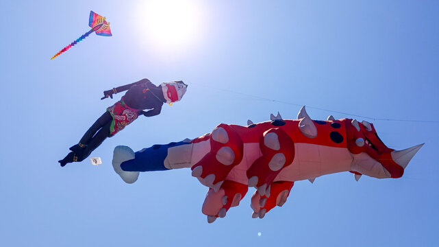 Surabaya, East Java, Indonesia - August 30th 2026: Colorful giant creative shape kites and traditional Indonesian character puppets flying in the clear blue sky during a summer festival.